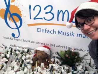 Musikschulleiterin Katharina O'Connor präsentiert vor dem 123musik-Logo viele Weihnachtsgeschenke