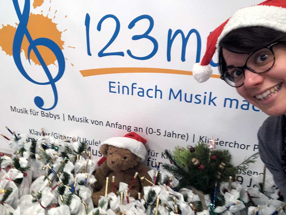 Weihnachtsgeschenke Musikschulleiterin Katharina O'Connor präsentiert vor dem 123musik-Logo viele Weihnachtsgeschenke