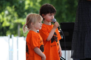 Zwei Kinder stehen auf einer Bühne und singen in ein Mikrofon.